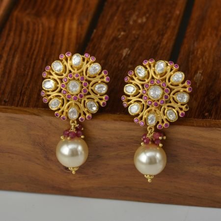 A sophisticated pair of gold earrings adorned with pearls and gemstones on wooden background.